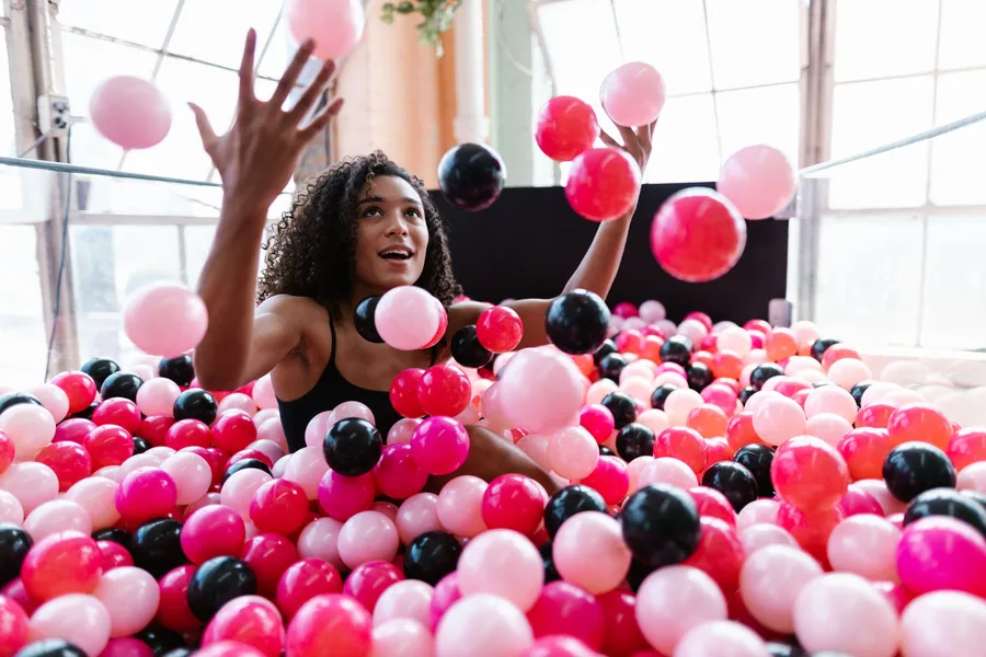 woman sitting in a ball pit pool and throwing plastic balls