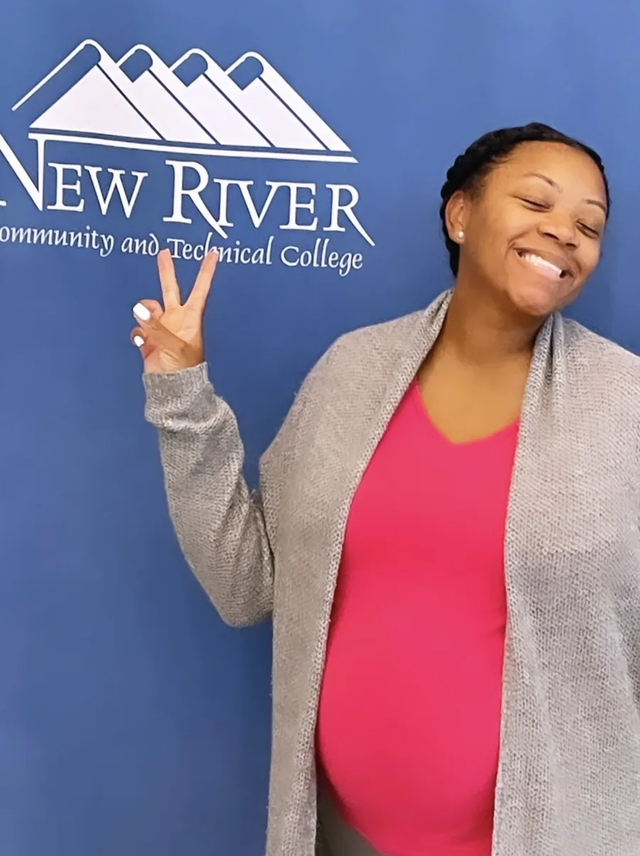 Marquisha smiling with a peace sign in front of a New River Community and Technical College banner